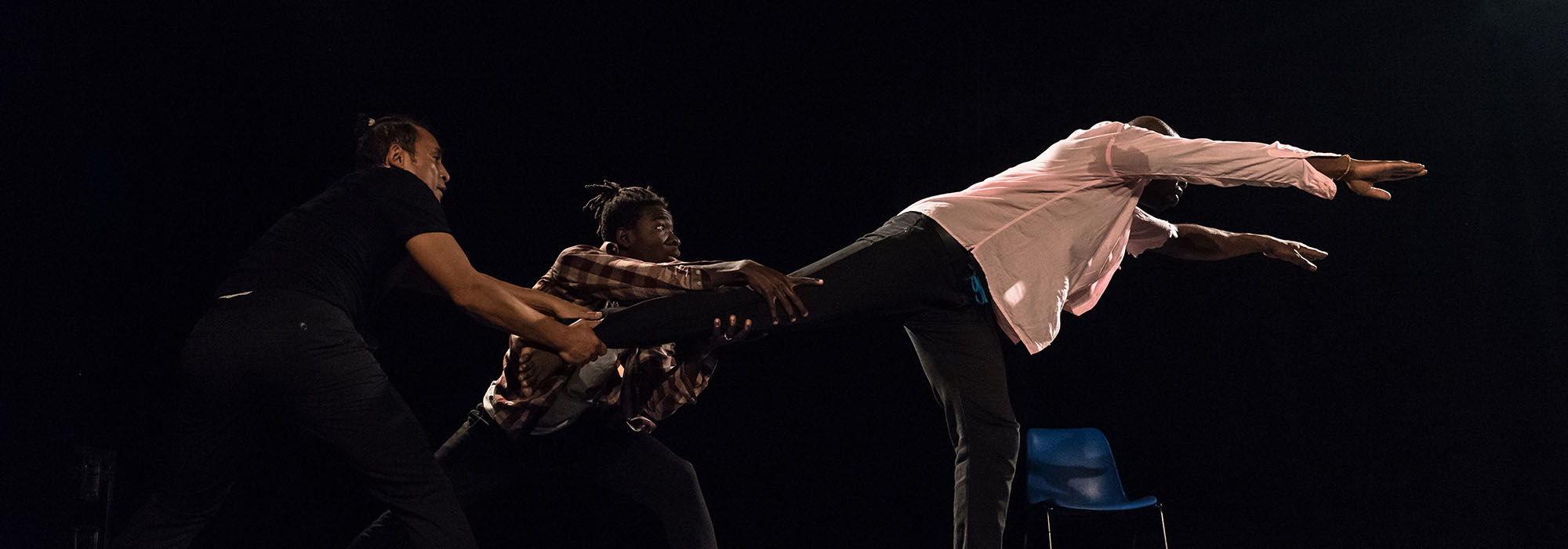 Pa Weogo, l'aventurier - Création compagnie Ouedmed Danse Trois danseurs sur scène, un des danseurs fait un mouvement comme pour s'enfuir en plongeant vers l'avant, les deux autres danseurs le retiennent par une jambe
